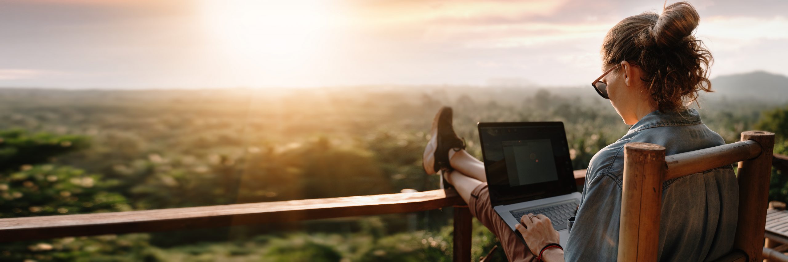 Young business woman working at the computer in cafe on the rock. Young girl downshifter working at a laptop at sunset or sunrise on the top of the mountain to the sea, working day.