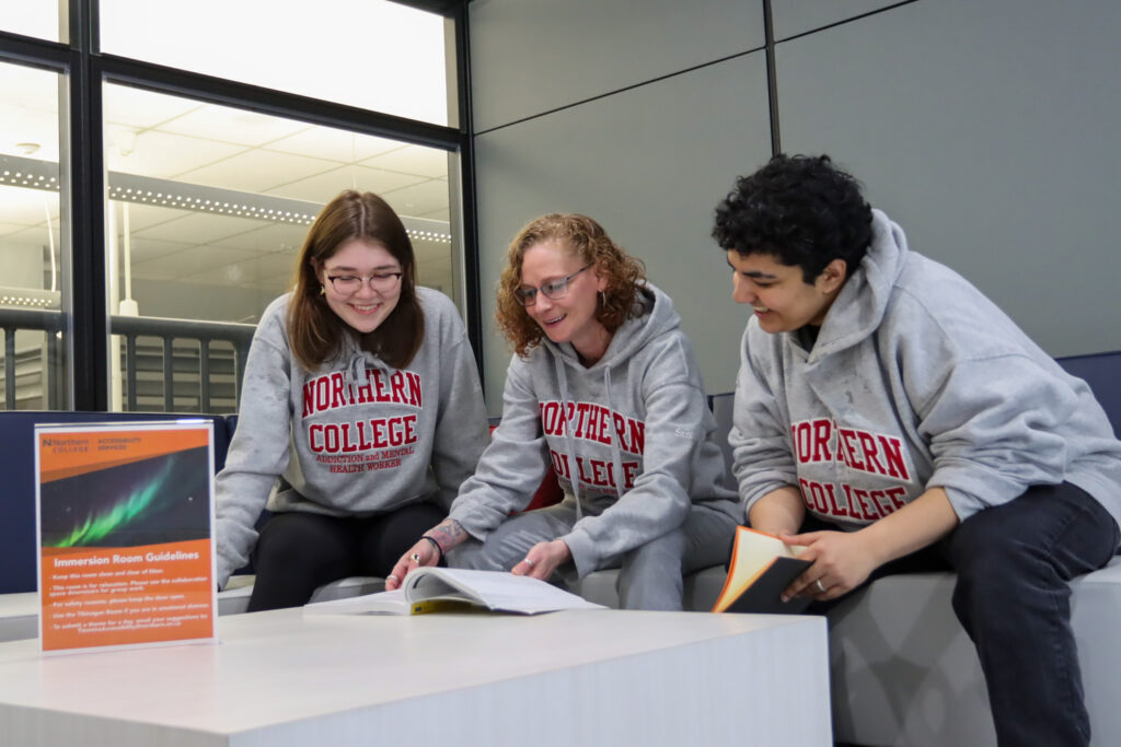 Group of Northern College students looking at textbook wearing Northern College swag