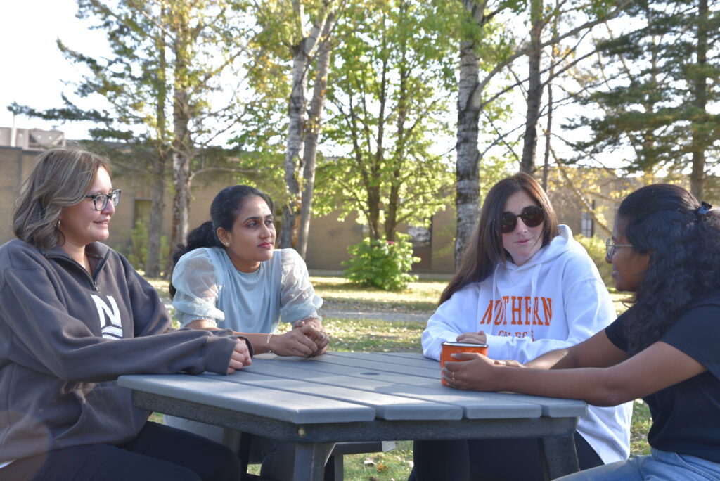 four at Northern College students sitting around picnic table outside of Timmins Campus