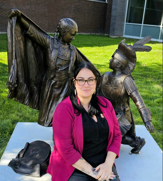 Every Child Matters statue at Timmins Campus with an indigenous lady sitting nearby