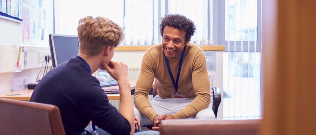 Male College Student Meeting With Campus Counselor Discussing Mental Health Issues