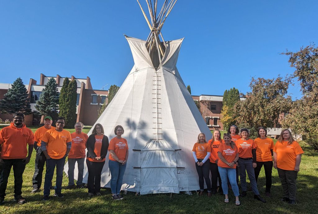 Photo of students and employees wearing orange outside tipi